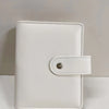 A white leather ring binder notebook with a stitched closure.