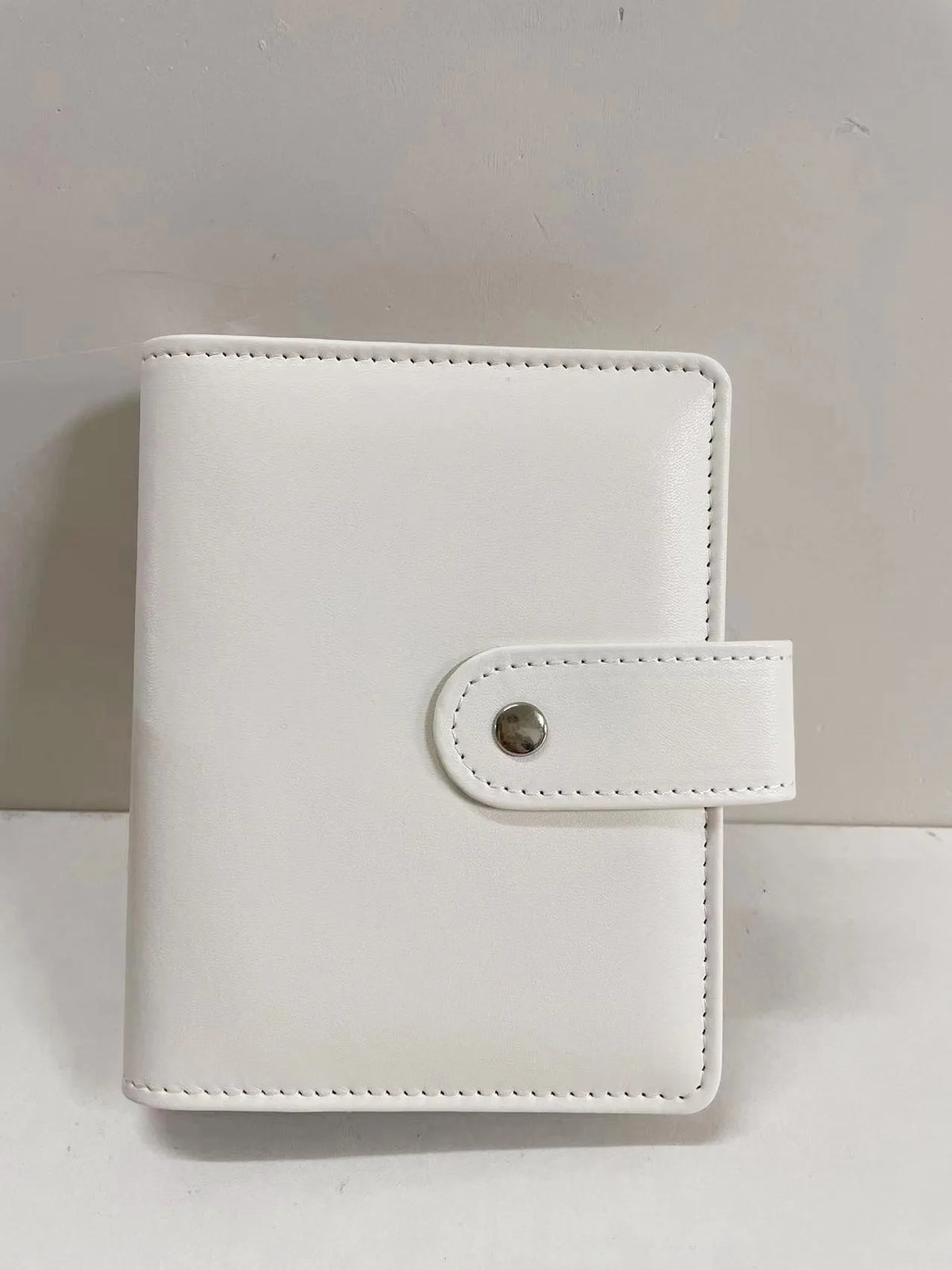 A white leather ring binder notebook with a stitched closure.