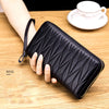 A black genuine leather RFID women's travel wallet with a zipper closure is held in a hand on a wooden surface.