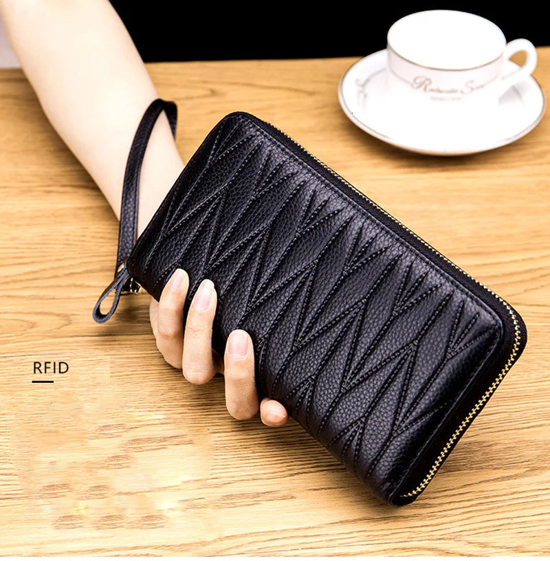 A black genuine leather RFID women's travel wallet with a zipper closure is held in a hand on a wooden surface.