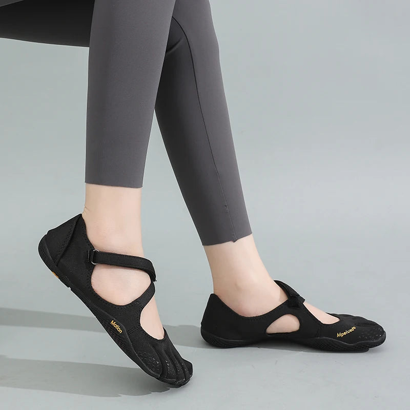 A pair of black women's barefoot five-toe shoes with an adjustable strap shown on a person's foot.