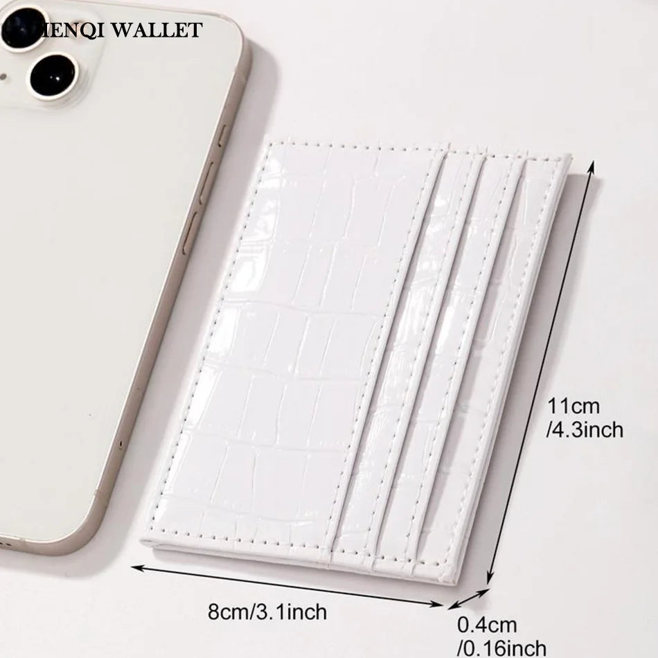 A white crocodile pattern slim card holder wallet next to a smartphone.