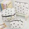 A collection of quilted white makeup bags with black trim and gold accents are displayed on a white surface.