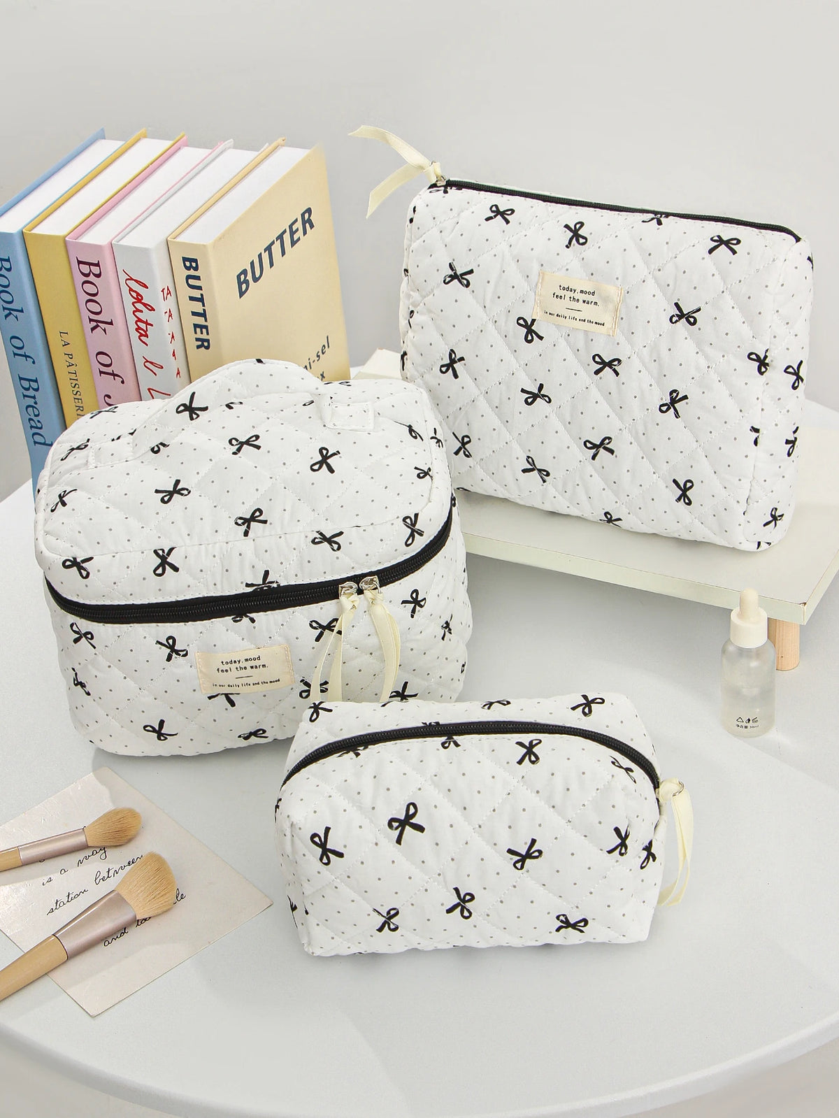 A collection of quilted white makeup bags with black trim and gold accents are displayed on a white surface.