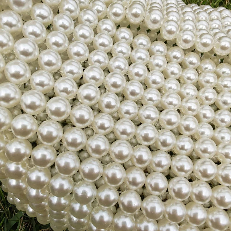 A close-up of a clutch bag covered entirely in small, round white pearls.