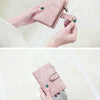 A hand holds a pink frosted card wallet with gold hardware and an emerald green accent.