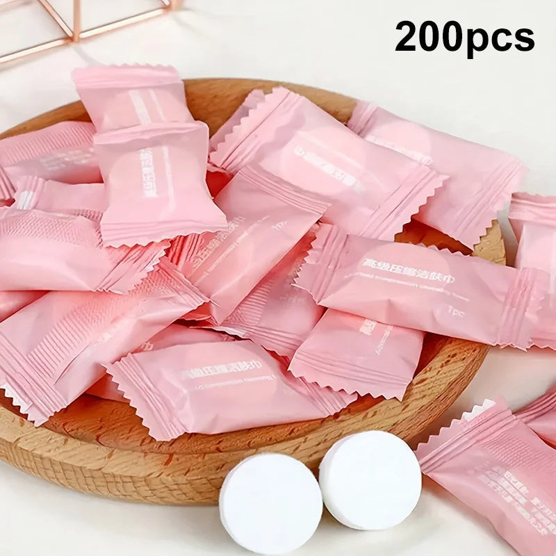Une pile de 200 serviettes faciales en coton compressé et réutilisables roses sont exposées sur une planche en bois.