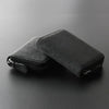 A black compact RFID-blocking card wallet with a zippered closure is shown lying on a dark surface.