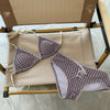 A purple gingham bikini set with a halter top and low-rise bottoms is displayed on a wooden hanger.