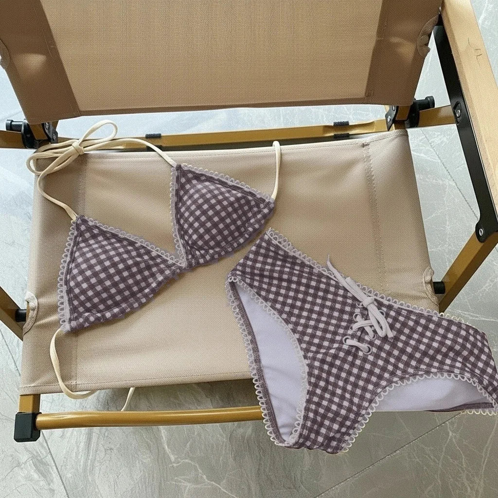 A purple gingham bikini set with a halter top and low-rise bottoms is displayed on a wooden hanger.