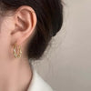 Goldene U-förmige geometrische Ohrringe, getragen im Ohr einer Frau.