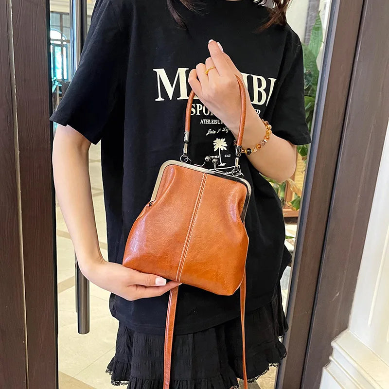 A woman holds a tan leather shell handbag with a gold chain strap against a dark background.