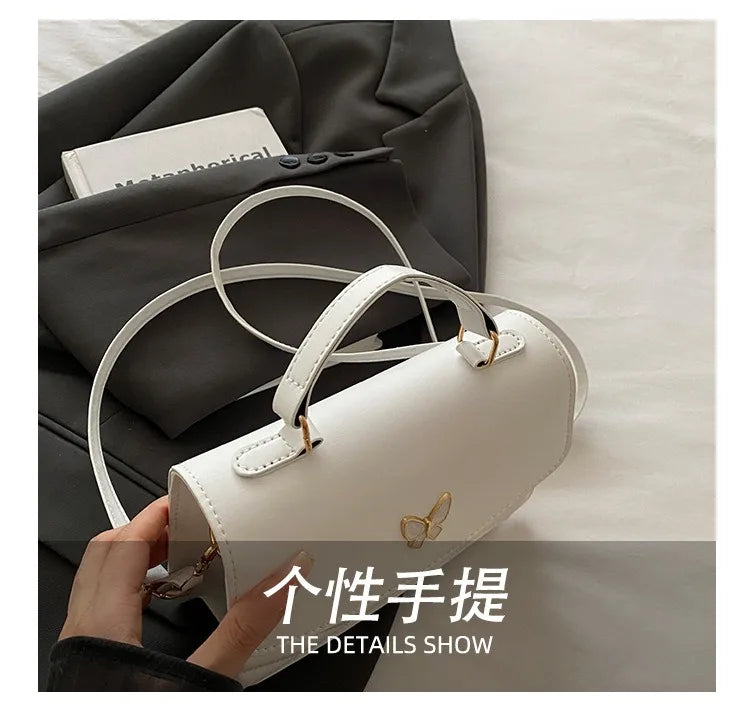 A white leather shoulder bag with gold hardware is shown resting on a dark gray fabric, highlighting its details.