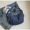 Dunkelblaue Nylon-Crossbody-Tasche auf einer Jeansjacke und einem Buch.