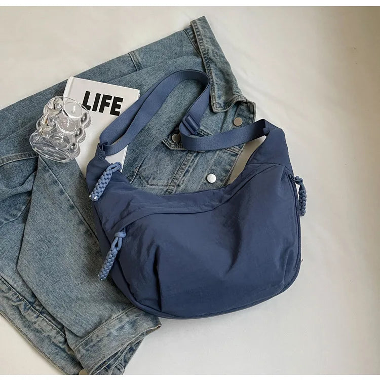 Dunkelblaue Nylon-Crossbody-Tasche auf einer Jeansjacke und einem Buch.