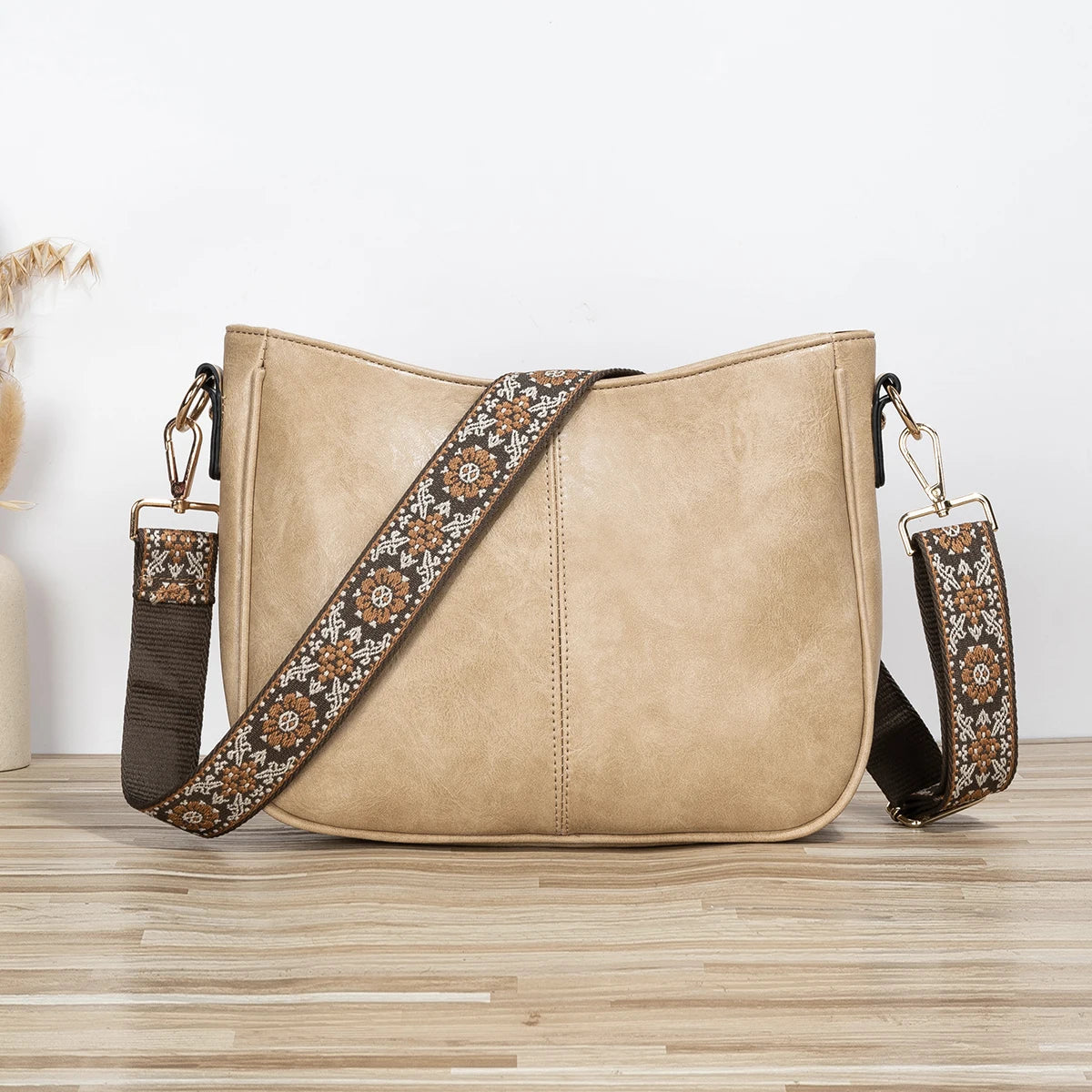 A tan PU leather shoulder crossbody bag with a brown patterned strap resting on a wooden surface.