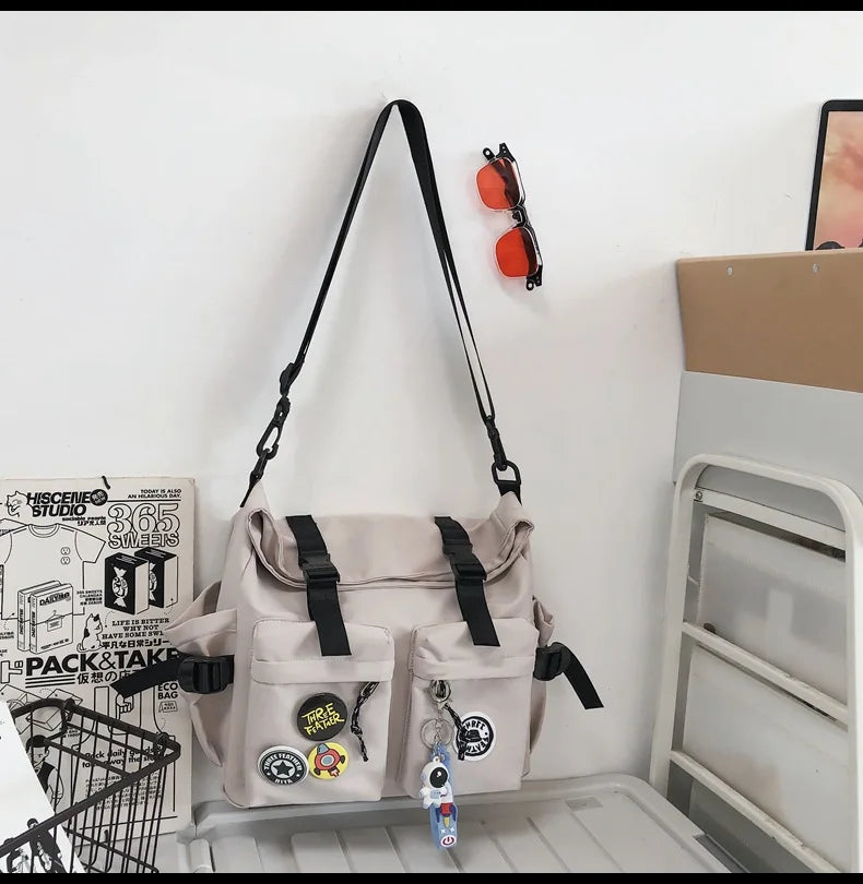 A beige nylon crossbody bag with black straps and orange accents is displayed next to a white storage rack.