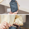 A hand holds a dark blue leather coin purse with a gold chain keychain against a light background.