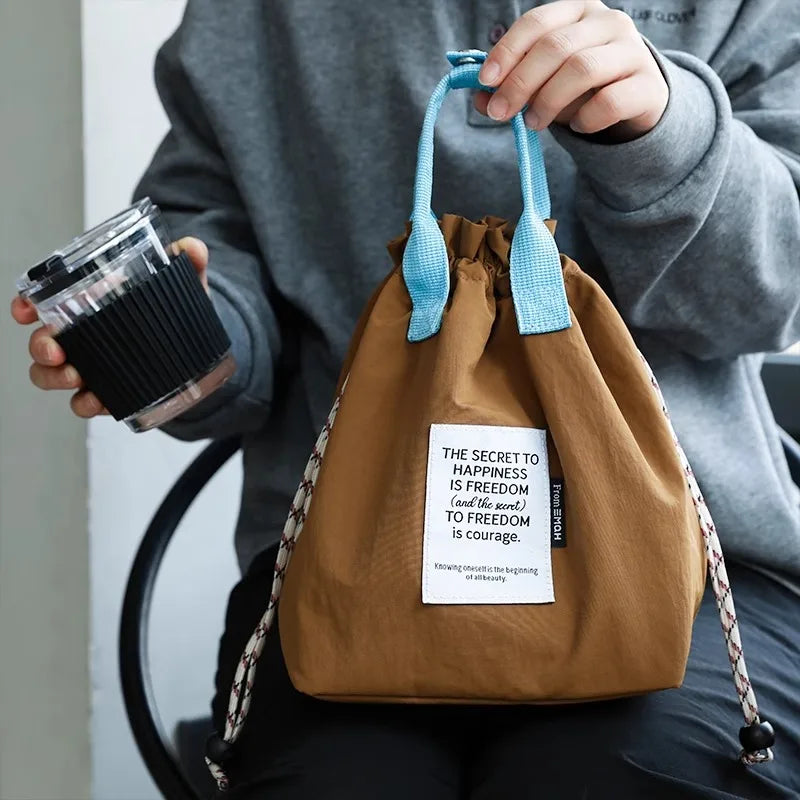 A person holds a brown waterproof insulated lunch bag with blue drawstrings against a gray background.