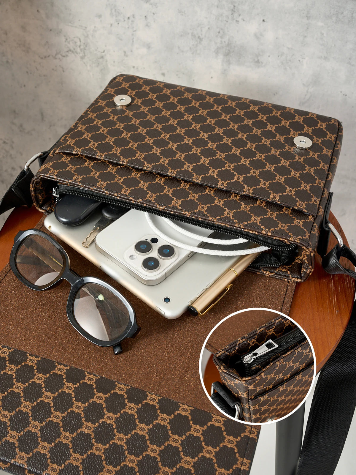A brown Gucci print flap crossbody bag is shown open, revealing a smartphone and sunglasses on a wooden surface.