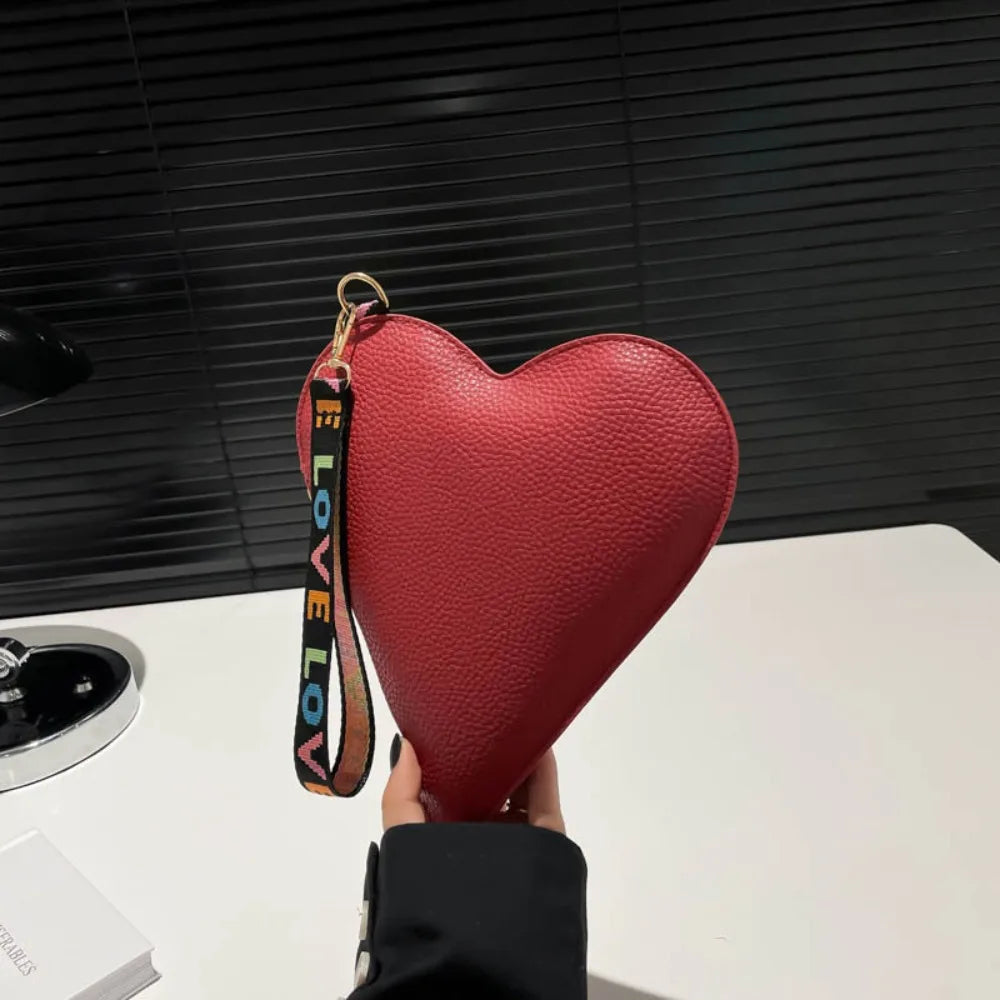 Cartera de monedas con forma de corazón roja intensa de PU y correa dorada, mostrada contra un fondo oscuro.