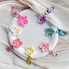 A collection of colorful resin flower keychains in pink, purple, and white are displayed on a white plate.