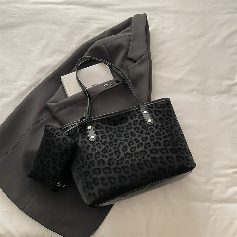 A black leopard print tote bag with gold hardware is placed on a gray suit jacket and a white shirt on a light surface.