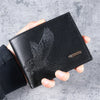 A black slim leather wallet featuring an embossed eagle design is held in a person's hand.