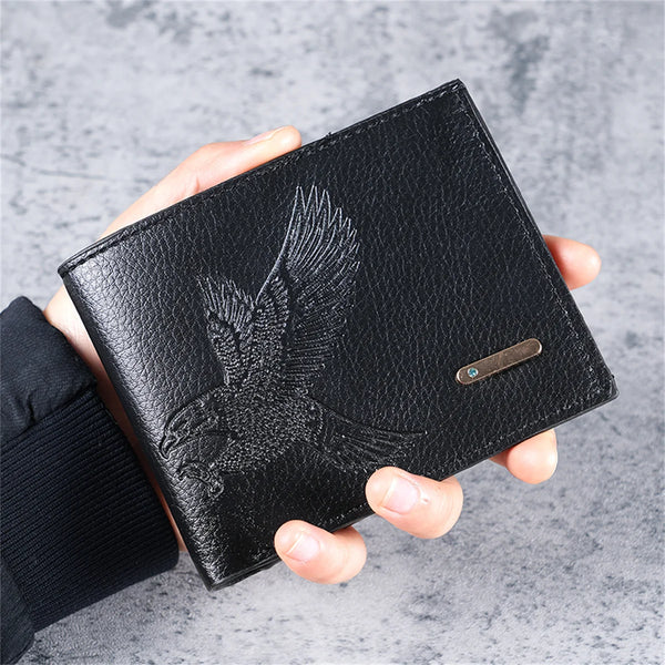 A black slim leather wallet featuring an embossed eagle design is held in a person's hand.