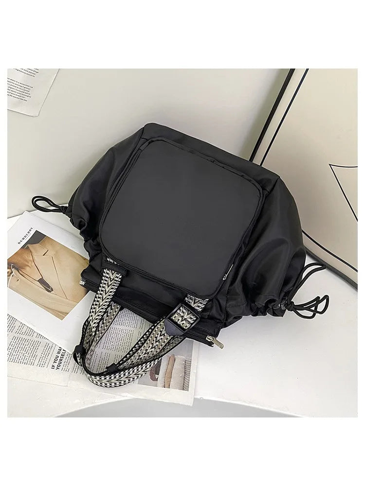 A black nylon shoulder bag with a square compartment and patterned fabric trim is shown on a white surface.
