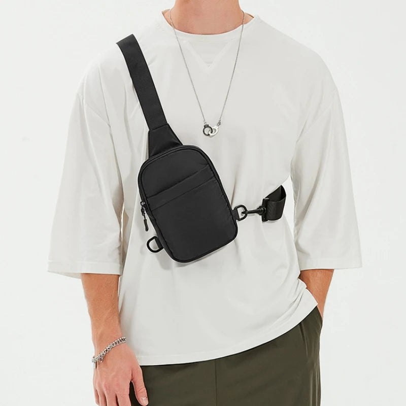 Una persona vistiendo una camiseta blanca muestra un bolso cruzado negro multifuncional con correa y clip.