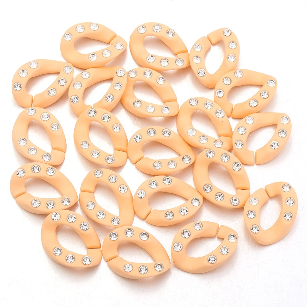 A collection of small, round, gold-colored acrylic link chain connectors with clear rhinestones.
