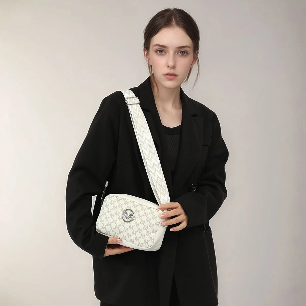 A woman models a white and gray retro M-pattern crossbody bag against a light gray background.
