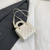 A light cream quilted crossbody handbag with a gold chain accent resting on a white surface next to a dark gray blazer.