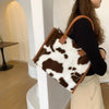 A woman holds a brown leather tote bag with a leopard print faux fur exterior in a light beige setting.
