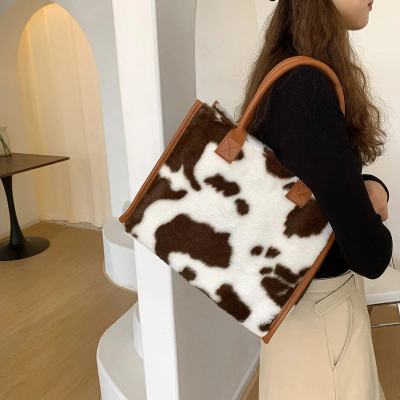 A woman holds a brown leather tote bag with a leopard print faux fur exterior in a light beige setting.