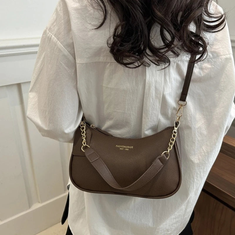 A brown leather shoulder bag with a gold chain pendant is shown against a white shirt.