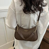 A brown leather shoulder bag with a gold chain pendant is shown against a white shirt.