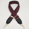 A close-up of a braided nylon bag strap in black and maroon checkered pattern with gold metal hooks.