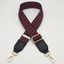 A close-up of a braided nylon bag strap in black and maroon checkered pattern with gold metal hooks.