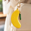 A yellow fruit-shaped coin purse keychain attached to a white leather handbag.