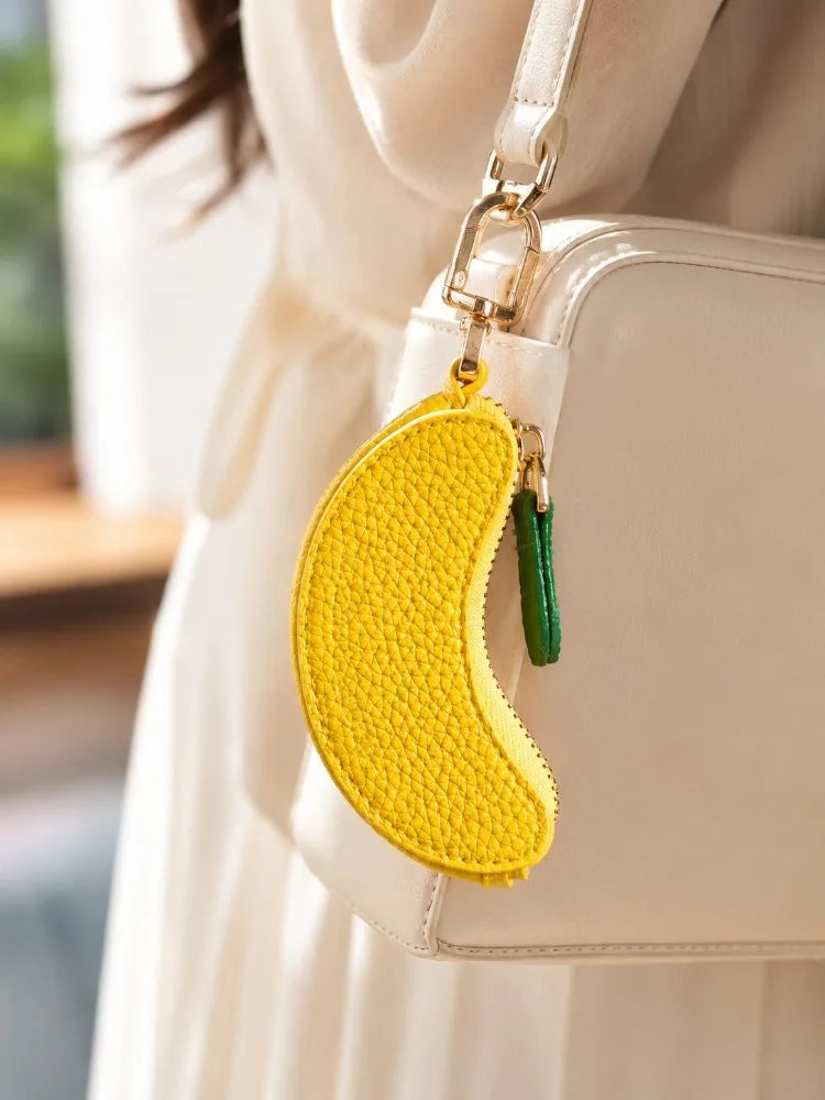 A yellow fruit-shaped coin purse keychain attached to a white leather handbag.