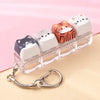 A set of five acrylic cat keycaps with various orange and white designs are displayed on a clear plastic bar with a silver ba