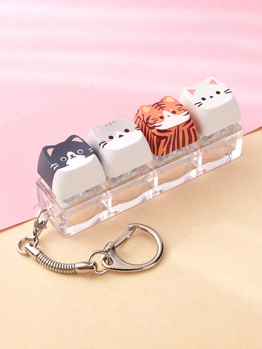 A set of five acrylic cat keycaps with various orange and white designs are displayed on a clear plastic bar with a silver ba
