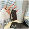 A hand holds a dark brown leather foldable mini keychain tote bag with a silver clasp against a light background.