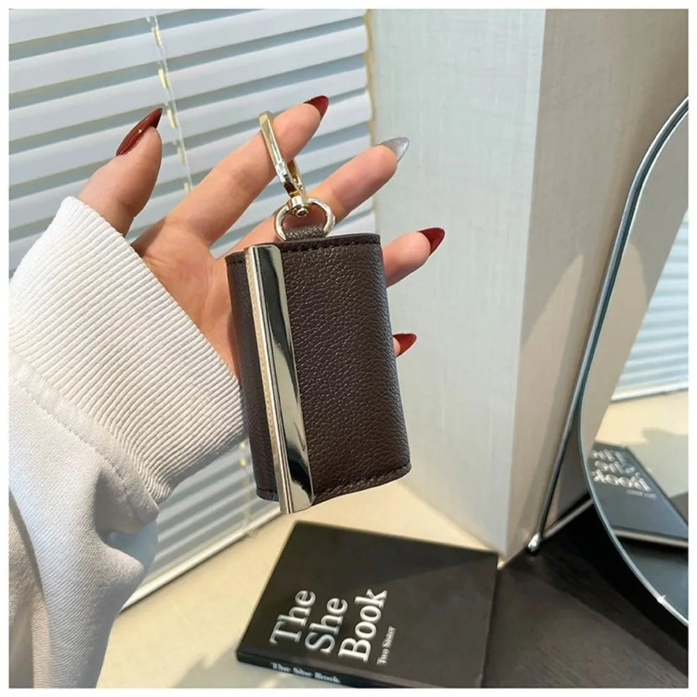 A hand holds a dark brown leather foldable mini keychain tote bag with a silver clasp against a light background.