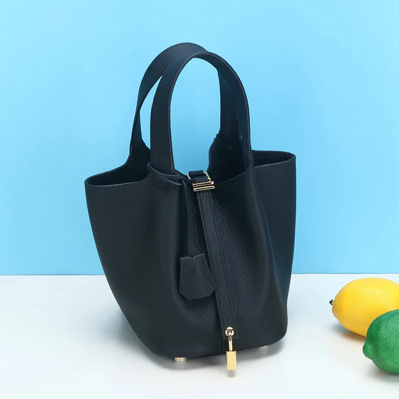Schwarze Ledikübeltasche mit goldener Reißverschlusverzierung auf weißem Hintergrund.