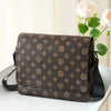 A brown men's casual crossbody bag with an easy flap design resting on a white surface next to pink roses.