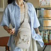 Helle beige Kunstleder-Crossbodytasche mit geflochtenem Riem, getragen von einer Person in einem blau gestreiften Hemd.