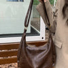A brown vintage PU leather tote bag with a crossbody strap is displayed on a wooden surface.
